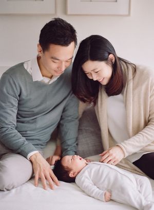 Loving parents smiling down at newborn baby lying on bed together.