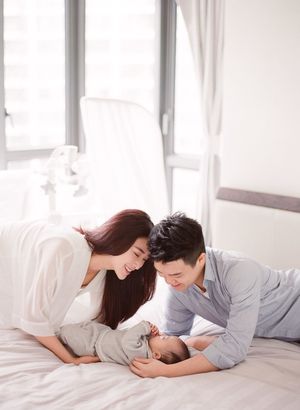 Loving parents lying on a white bed smiling at their newborn baby in soft natural light.