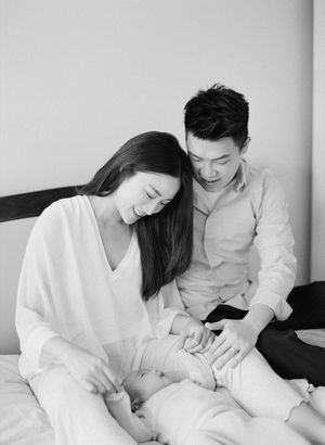 Smiling couple in white clothing tenderly caring for their newborn baby on a bed.