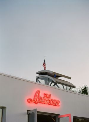 Glowing red neon sign for The Lobster restaurant with an American flag on the rooftop at dusk.