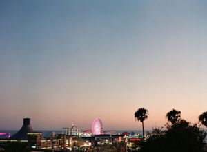 Colorful sunset skyline view of Santa Monica Pier with a Ferris wheel and palm trees silhouetted.