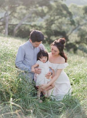 Asian family of three sitting together in a lush green meadow sharing a joyful moment.