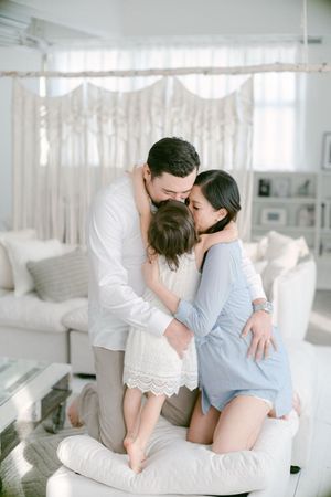 Loving family of three sharing a warm group hug in a bright white living room.