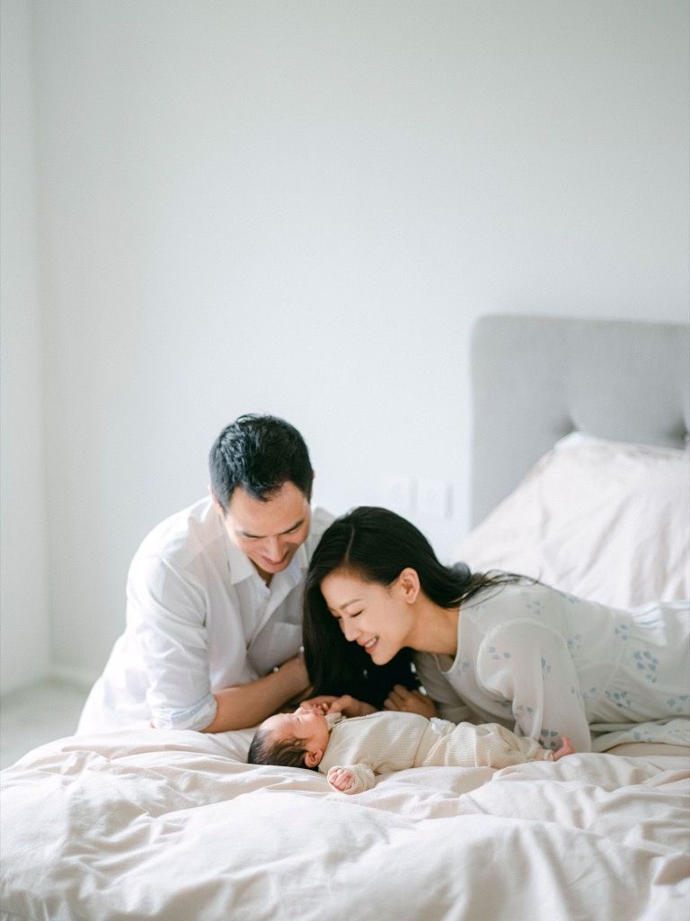 Parents lovingly gazing at their newborn baby lying on a white bed.