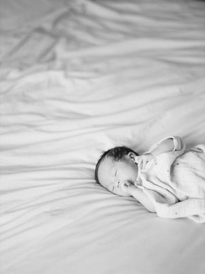 Peaceful newborn baby sleeping on white bed sheets in black and white photo.