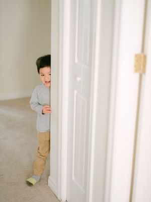 Curious toddler boy peeking playfully from behind a white door.