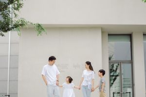 A family of four holding hands outdoors near a modern building, dressed in coordinating white outfits.