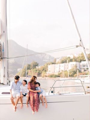 A family of four sitting together on the deck of a sailboat with a scenic coastal backdrop.
