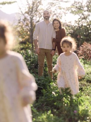 A couple stands smiling in a sunlit garden while two young children play in the foreground.