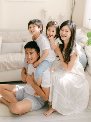 Happy Asian family of four posing together in bright cozy living room.