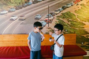 Two boys eating ice cream in front of a vintage highway mural indoors.