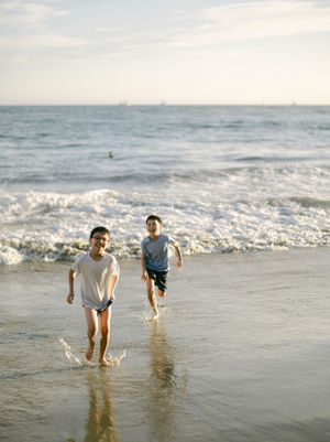 Two boys laughing and running through ocean waves on a sunny beach.