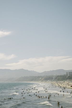 Crowded Santa Monica beach with mountains in the background on a hazy day.