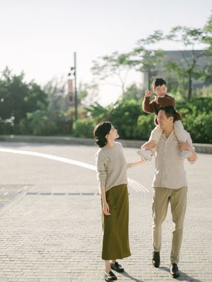 Happy Asian family with child on fathers shoulders walking in sunny outdoor plaza.