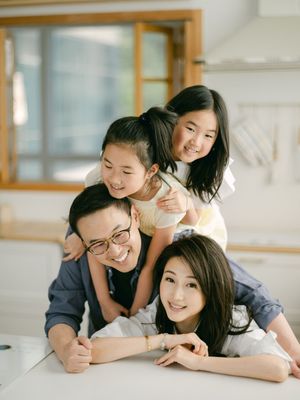 Joyful Asian family of four stacking up and smiling together in a bright modern kitchen.