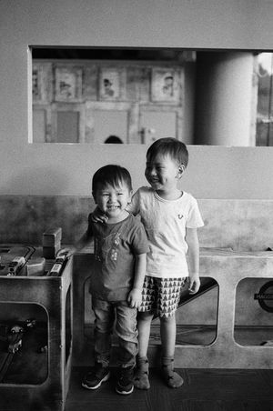 Black and white photo of two young brothers smiling and hugging inside a casual indoor setting.