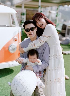 Young Asian family smiling together outdoors near vintage VW bus with baby.
