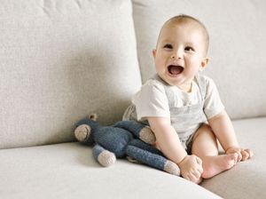 Happy laughing baby sitting on couch with stuffed monkey toy.
