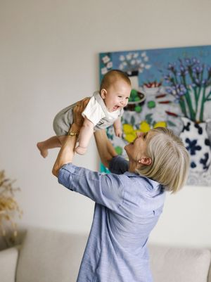 Grandmother joyfully lifting laughing baby in bright living room with colorful artwork.