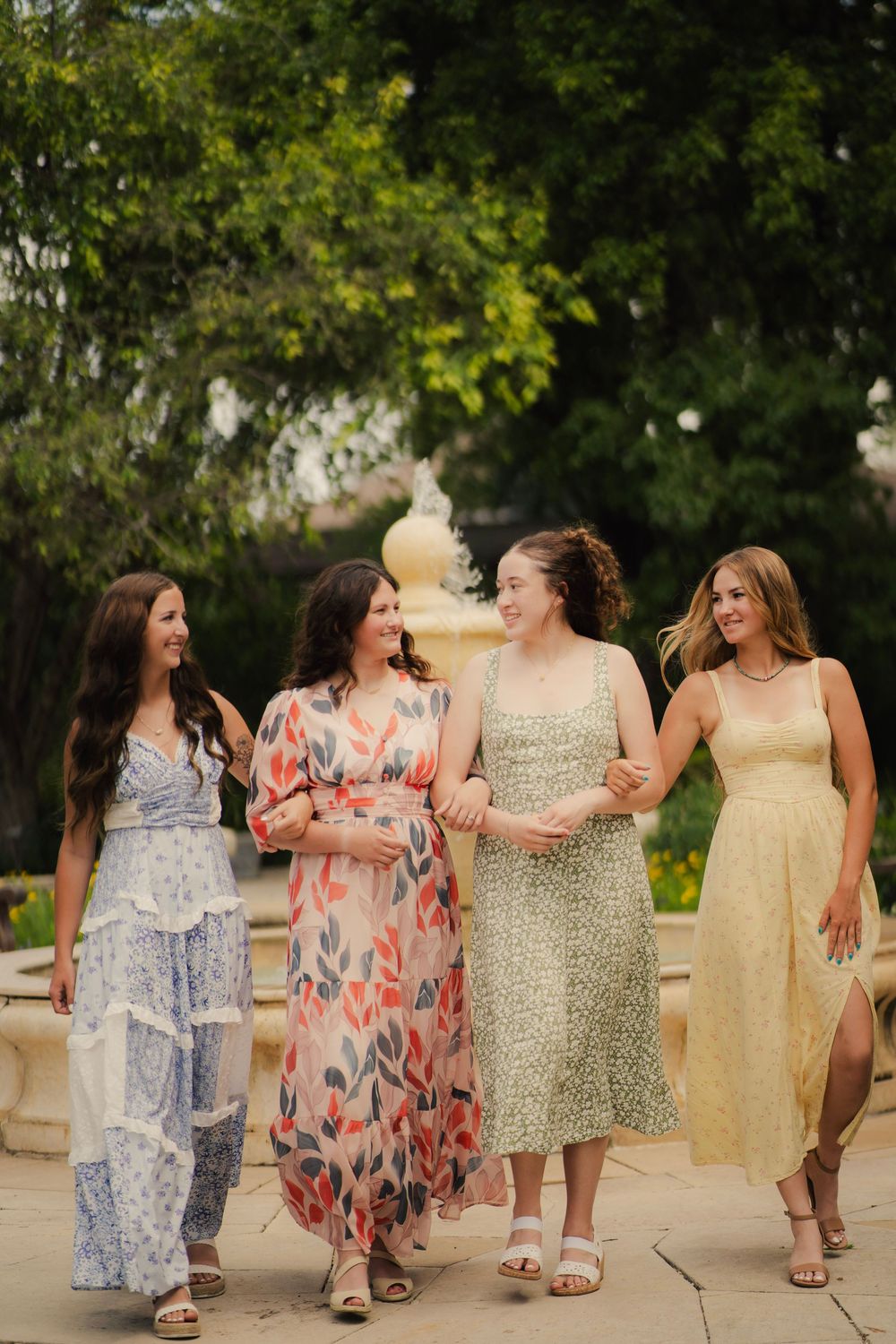 Four women in colorful summer dresses walking together and laughing in an outdoor garden.