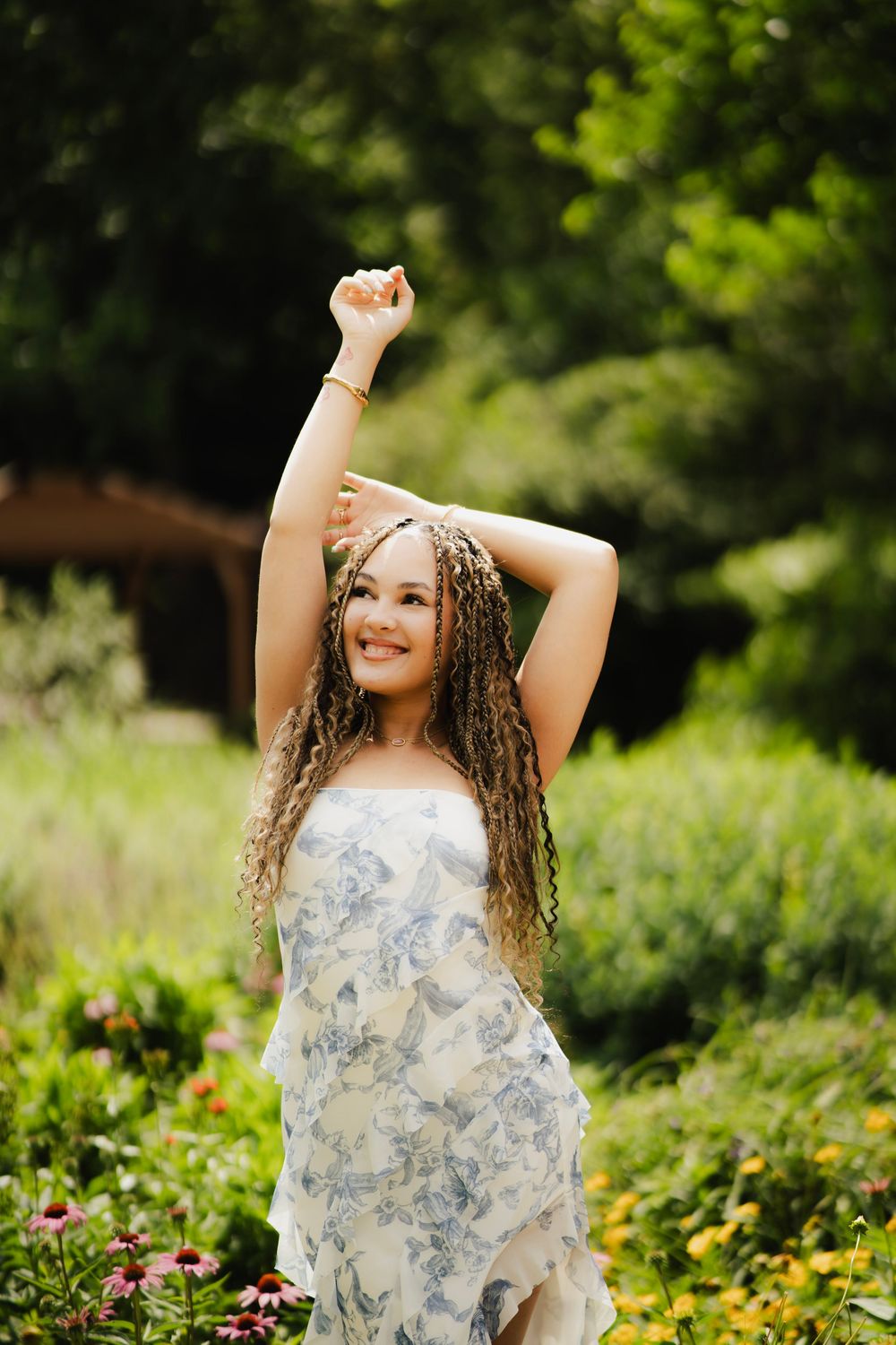 Young woman in blue floral dress raising her arm joyfully in a lush green garden.