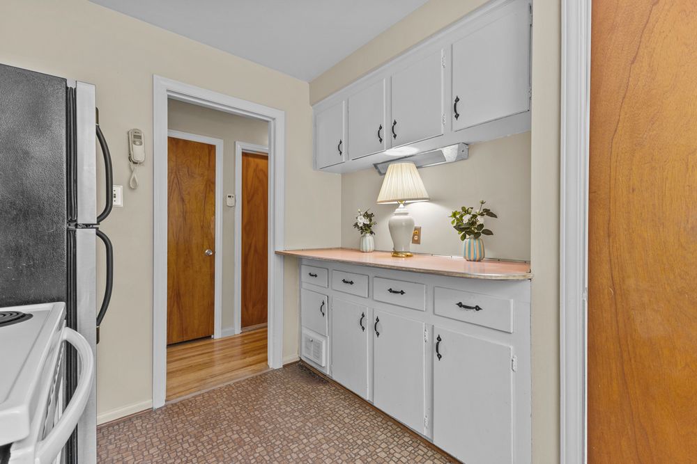 Kitchen area with white cabinets, light countertop, under-cabinet lighting, and wood-tone door leading to hallway.
