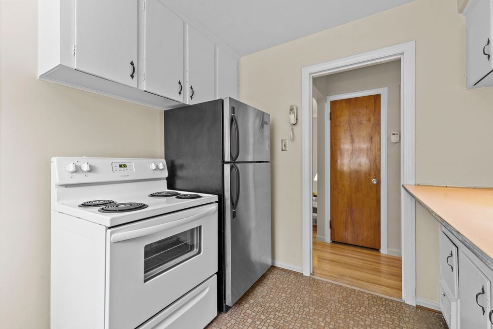Kitchen with white electric range, stainless refrigerator, white upper cabinets, and wood-tone door to adjacent room.