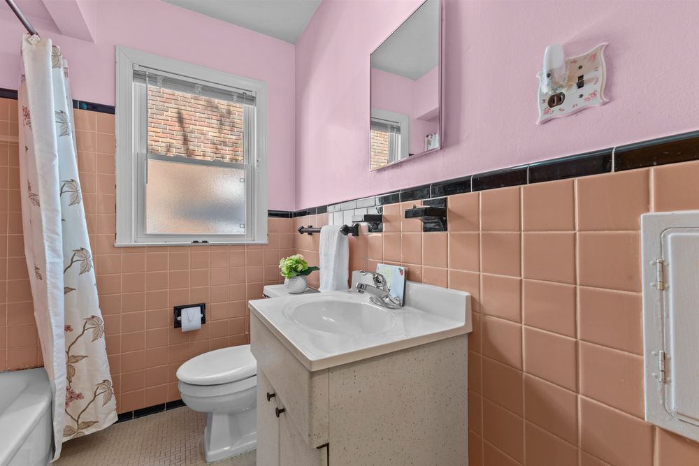 Vintage pink bathroom with peach tile walls, white vanity, toilet, and shower curtain.