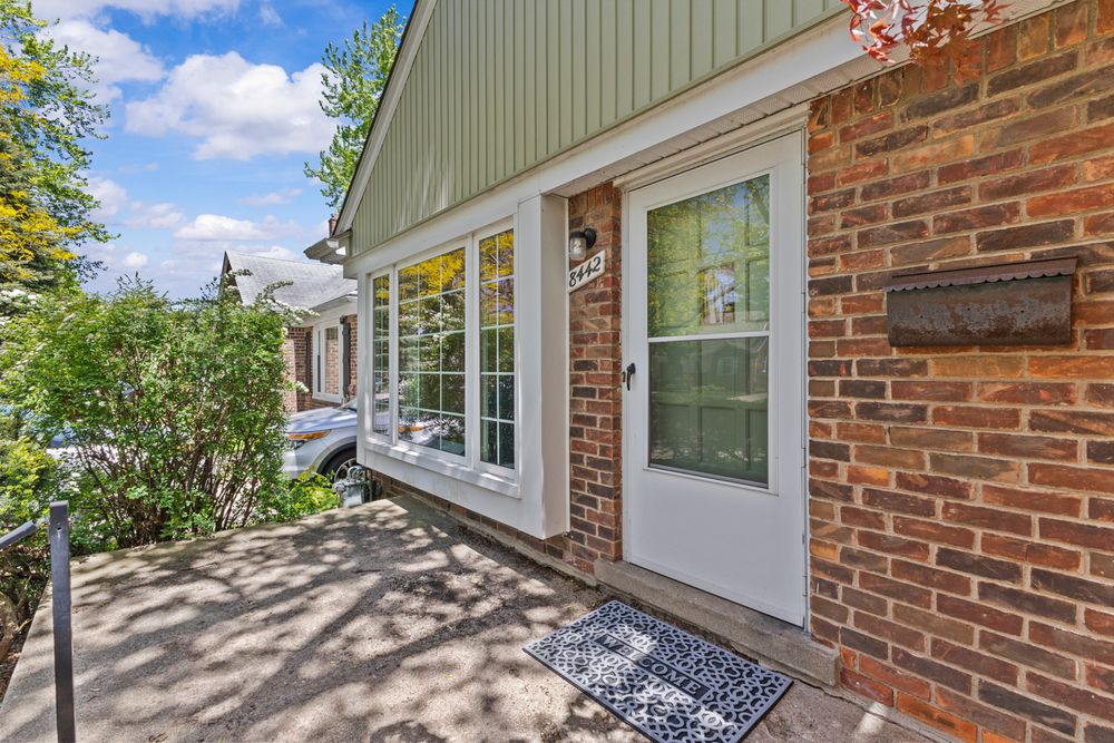 Brick home exterior featuring white front door, large window, and decorative welcome mat on porch.