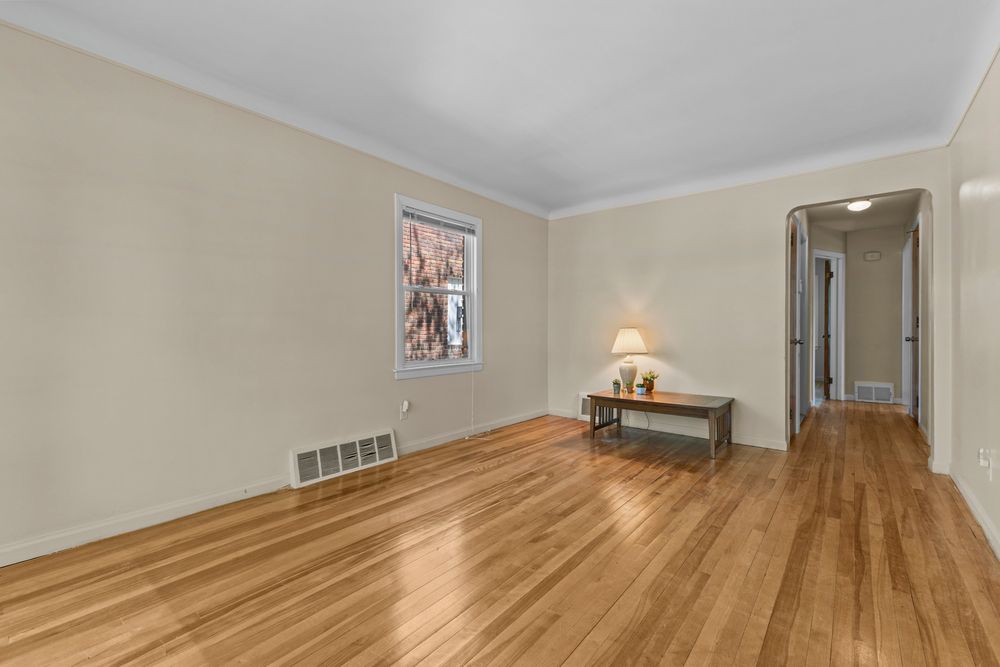 Bright living room with hardwood floors, crown molding, neutral walls, floor vent, and a small accent table near the window.