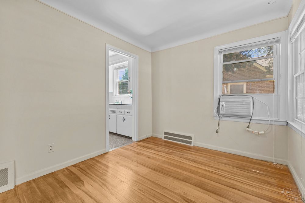 Empty bedroom with hardwood floors, crown molding, two windows, floor vent, and a wall-mounted AC unit.