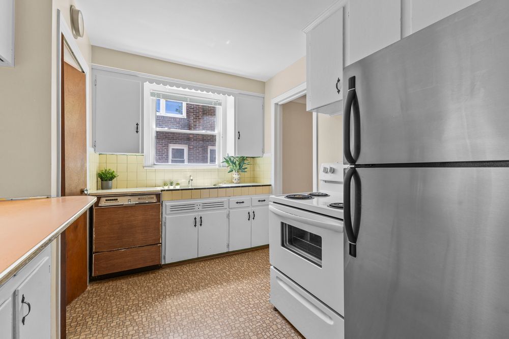 Galley kitchen with white cabinets, tile backsplash, stainless dishwasher, white range, and stainless refrigerator.