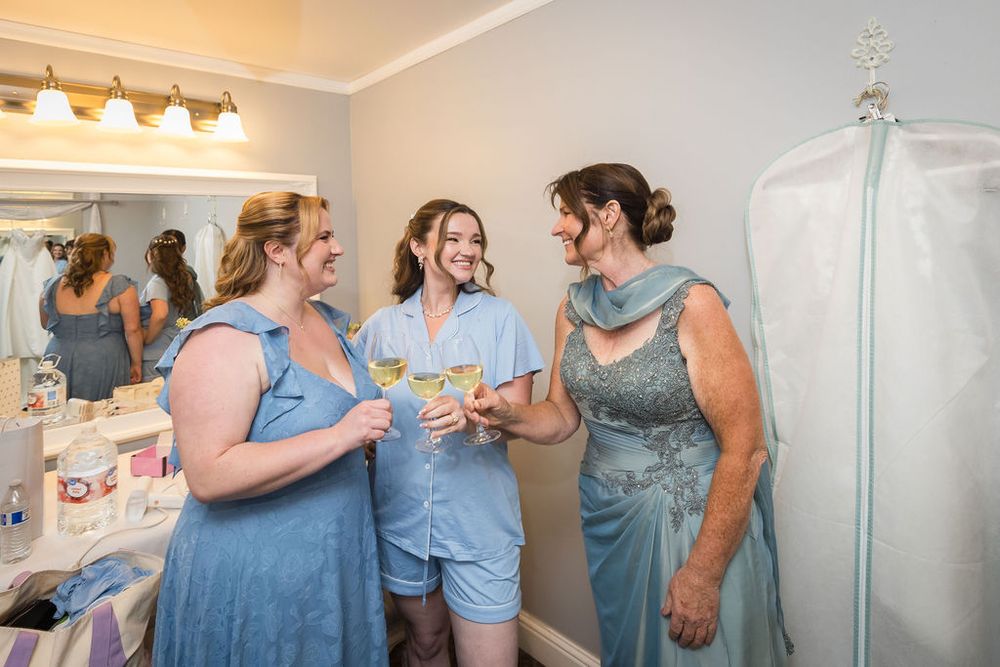 Bridesmaids in blue dresses toast with champagne while getting ready in bridal suite.