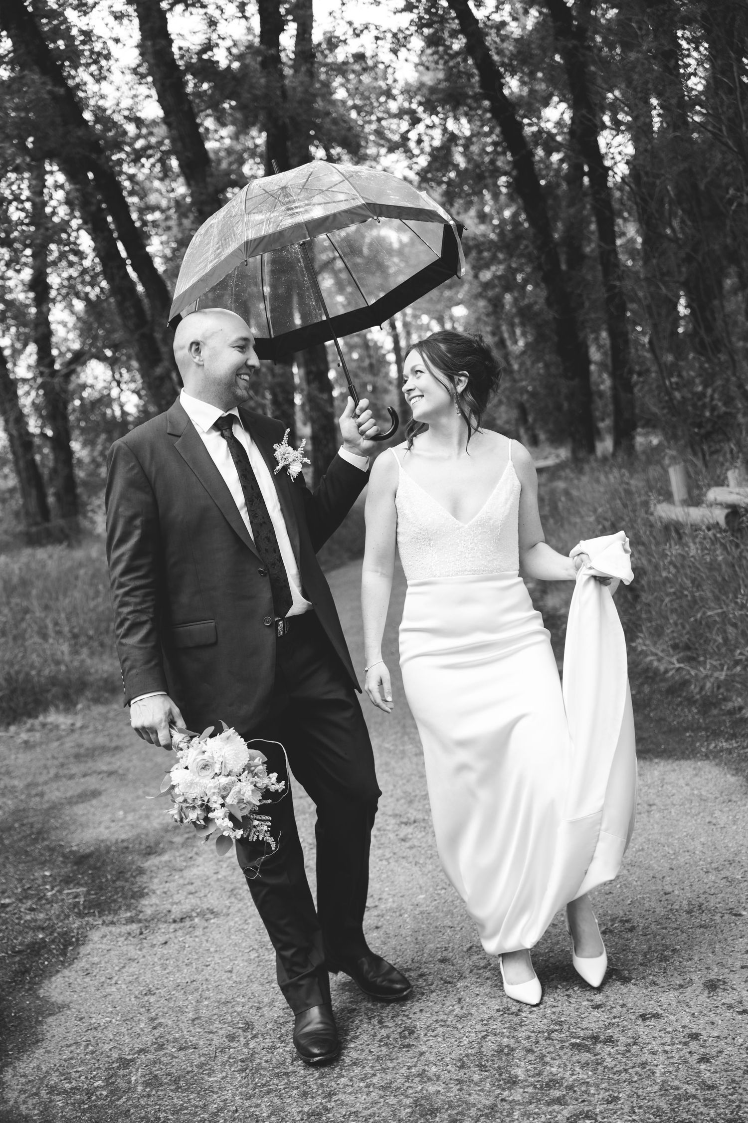 Black and white photo of bride and stylist reviewing wedding dress hanging by arched windows with scenic water view.