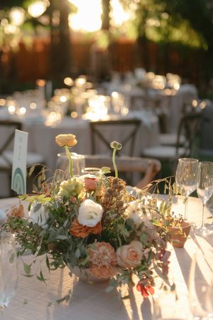 Elegant outdoor wedding reception with floral centerpiece of peach roses and greenery, glowing in warm golden sunset light.