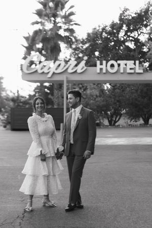 Black and white photo of a couple in wedding attire holding hands outside the Capri Hotel.