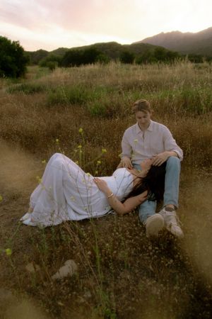 Romantic couple relaxing together in wildflower meadow at sunset with mountains behind.