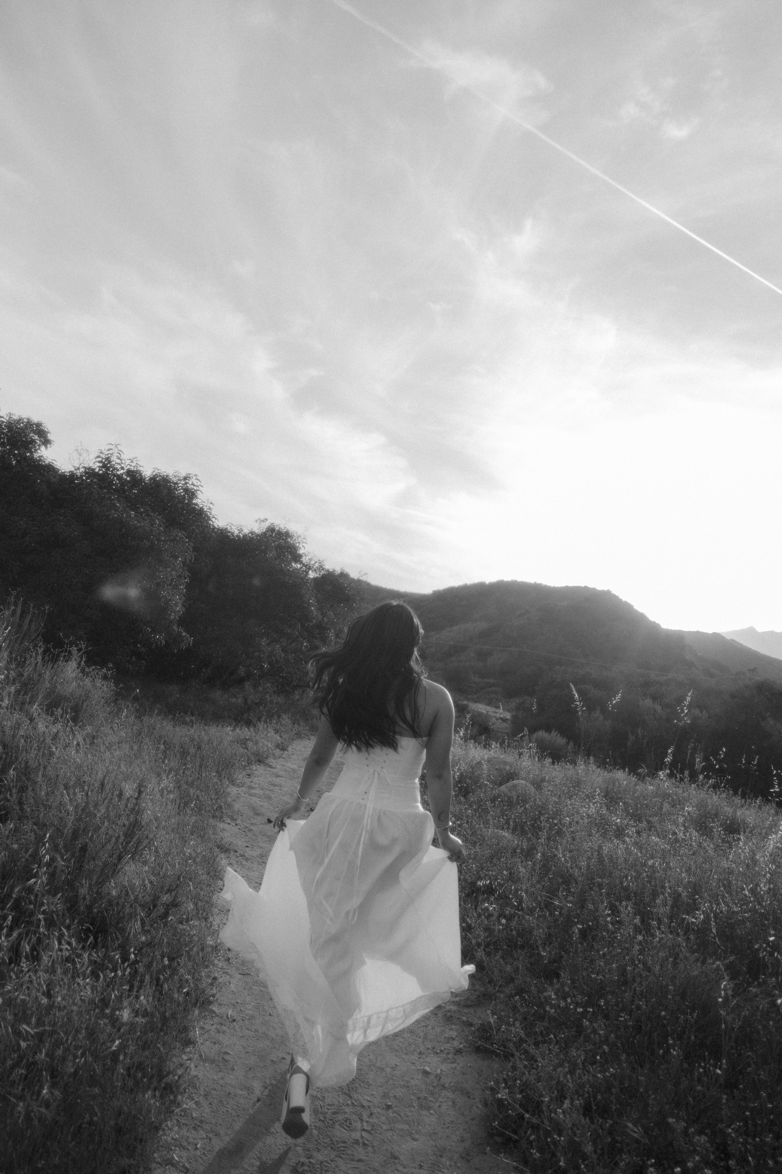 Woman in white dress running along mountain trail in black and white photography.