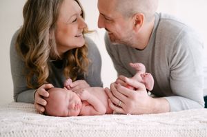 New parents smiling at their sleeping newborn baby lying on white knit blanket.