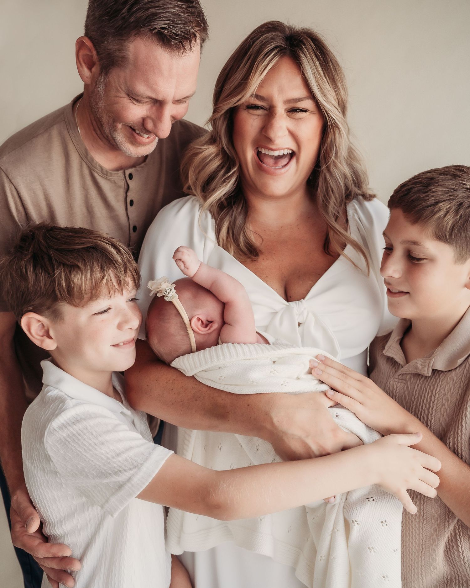 Happy family of five with parents, two boys, and a newborn baby girl posing together in a bright studio photo.
