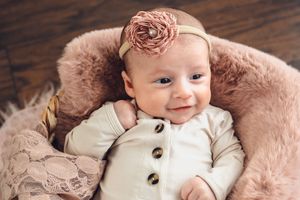 Adorable baby girl in floral headband smiling while lying in soft pink basket.