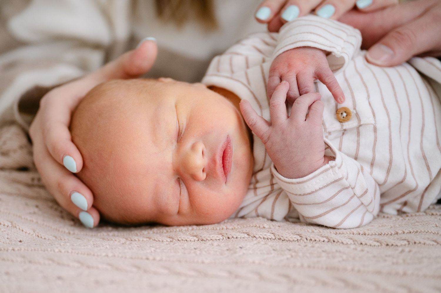Sleeping newborn baby in striped onesie cradled by mother with light blue nails.