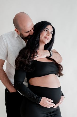 Pregnant couple embracing, man kissing woman's neck as she holds baby bump.