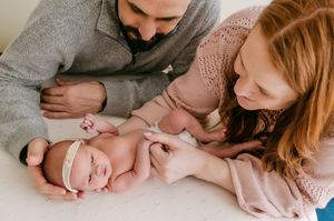 Parents lovingly gazing at their newborn baby girl wearing a pink headband.