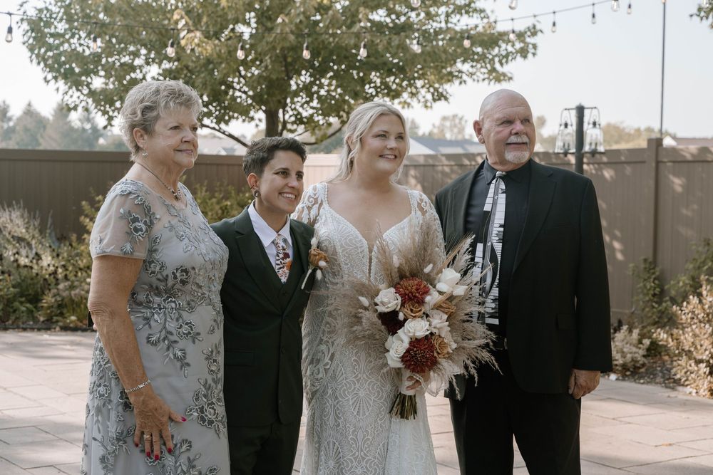Bride holding a bouquet poses with three family members outdoors at a wedding reception venue.