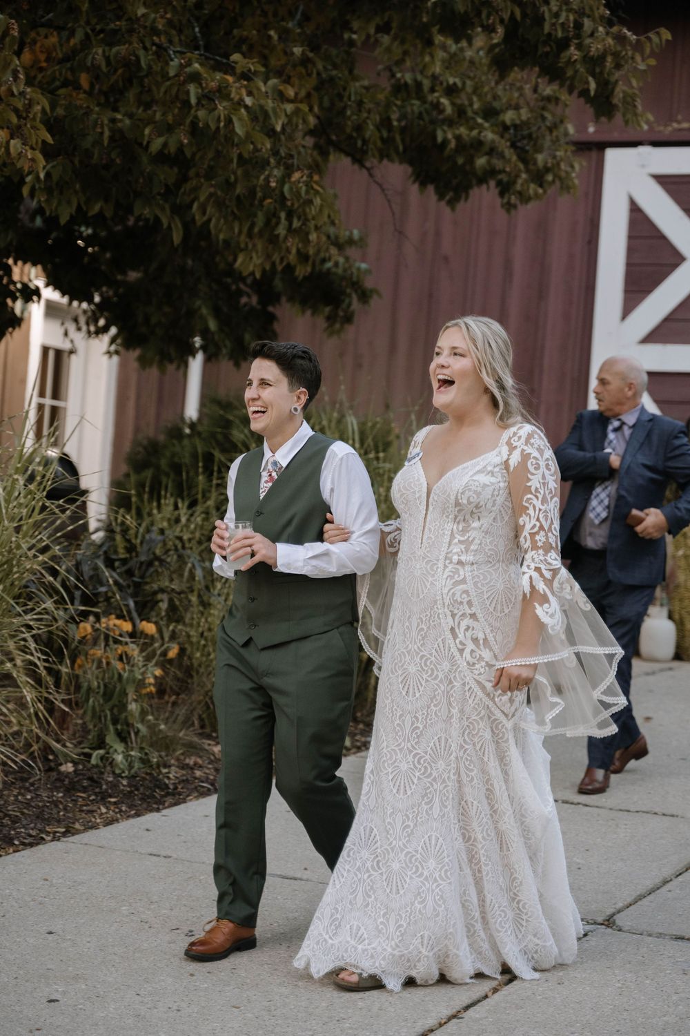 Joyful newlywed couple walking arm in arm after ceremony, bride in lace gown, partner in green suit.