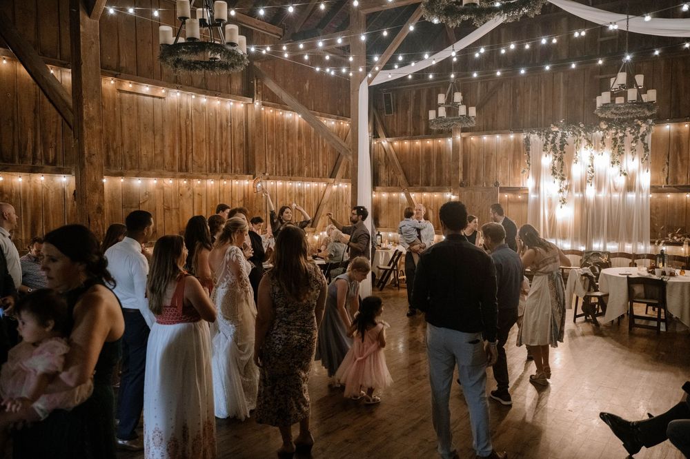 Guests dancing and celebrating at a rustic barn wedding reception with warm string lights and wooden walls.