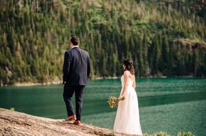 Bride and groom stand together overlooking a stunning turquoise mountain lake surrounded by forest.