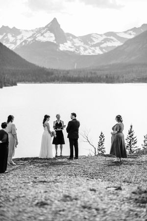 Outdoor wedding ceremony by mountain lake with snowy peaks in black and white.