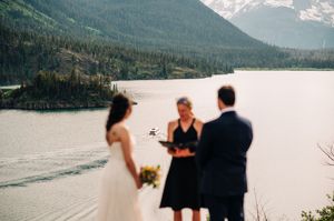 Couple exchanging vows outdoors with officiant by a scenic mountain lake.